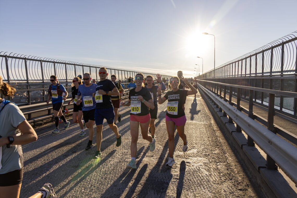 Runners take part in the Midnight Sun Marathon in Tromsø, crossing a bridge in bright evening sunlight.