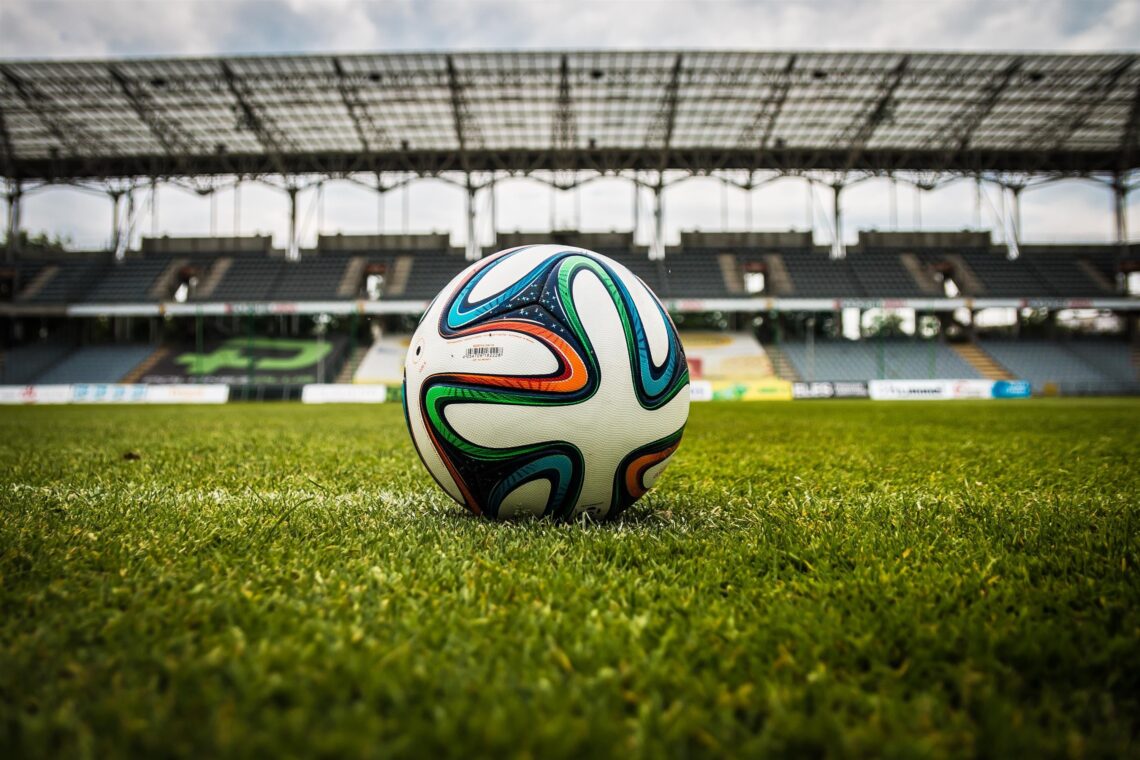 Soccer ball resting on green grass inside an empty football stadium.